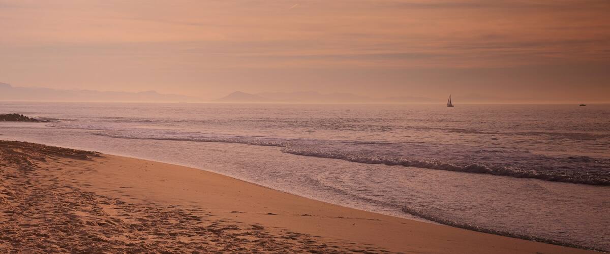A beach with waves, a sandy shore, and sailboats in the distance.