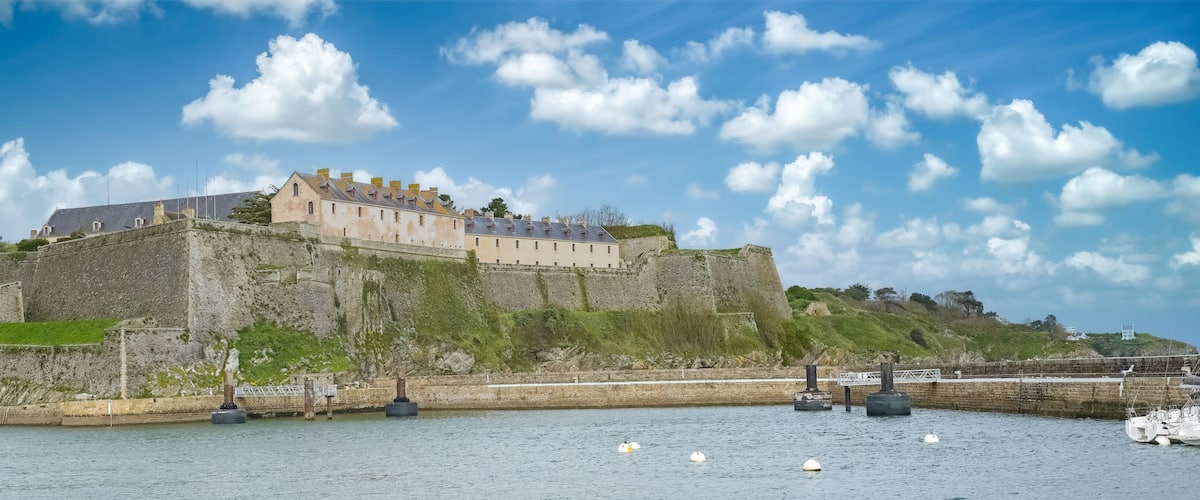 A historic castle on a hill overlooking a harbor with boats.