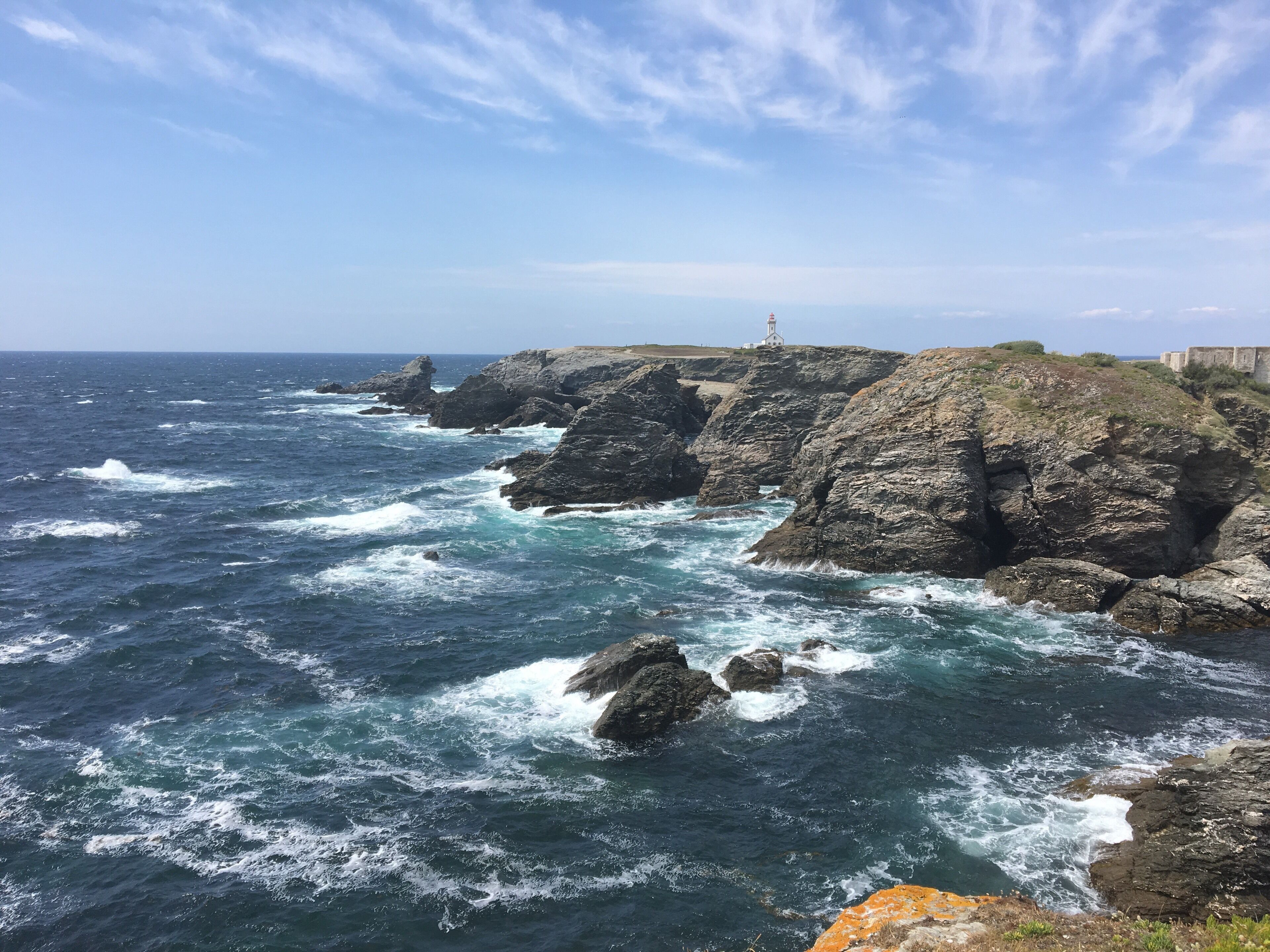 A rocky coastline with waves crashing against the rocks and a lighthouse in the distance.