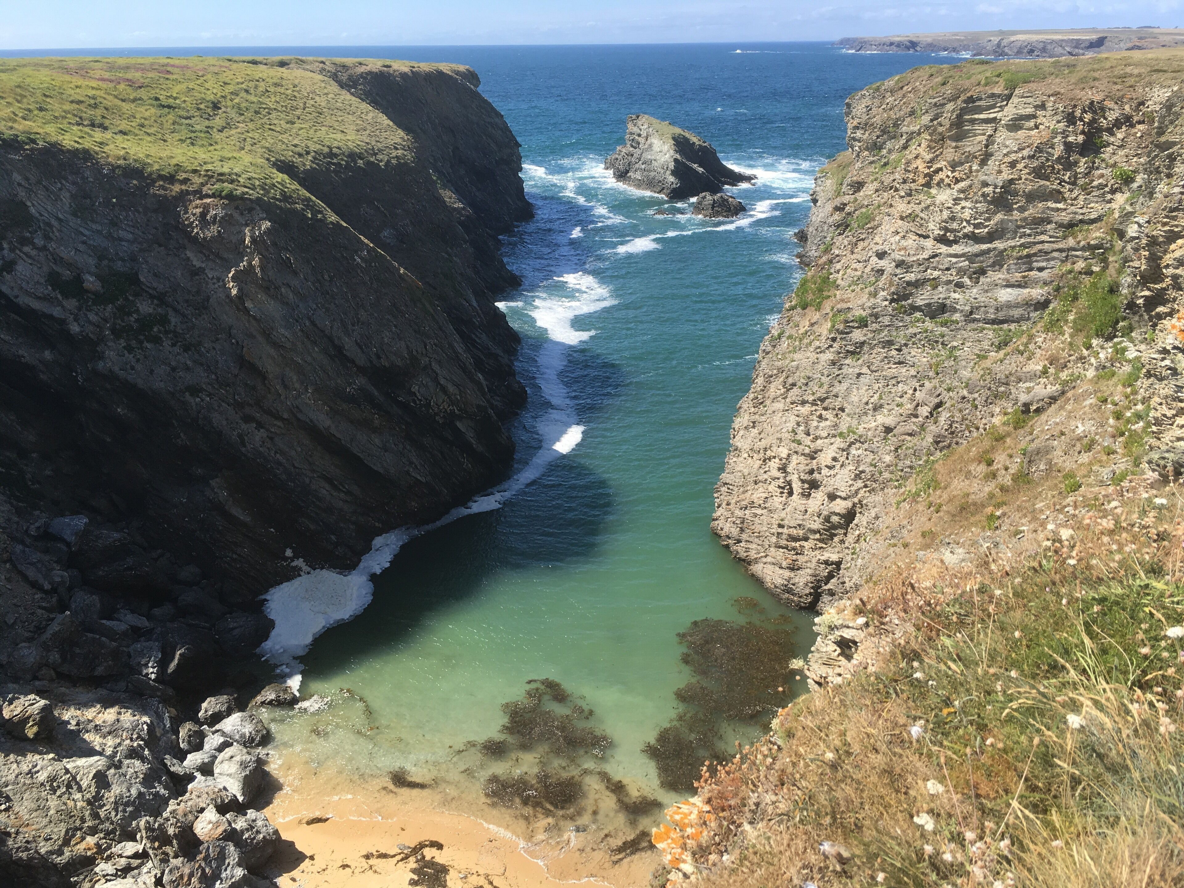 A coastal landscape with cliffs, a narrow beach, and clear blue waters.