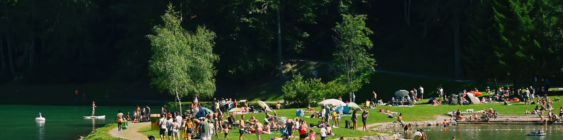 Un lago rodeado de bosque denso, con gente practicando diversas actividades como nadar y hacer paddleboarding.