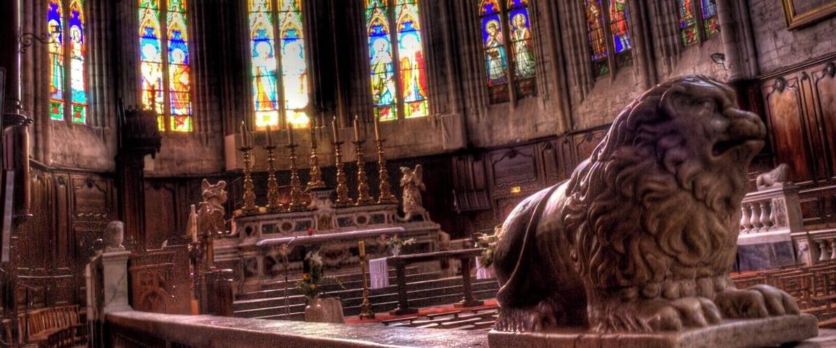 A cathedral interior with stained glass windows, a stone lion statue, and a high vaulted ceiling.