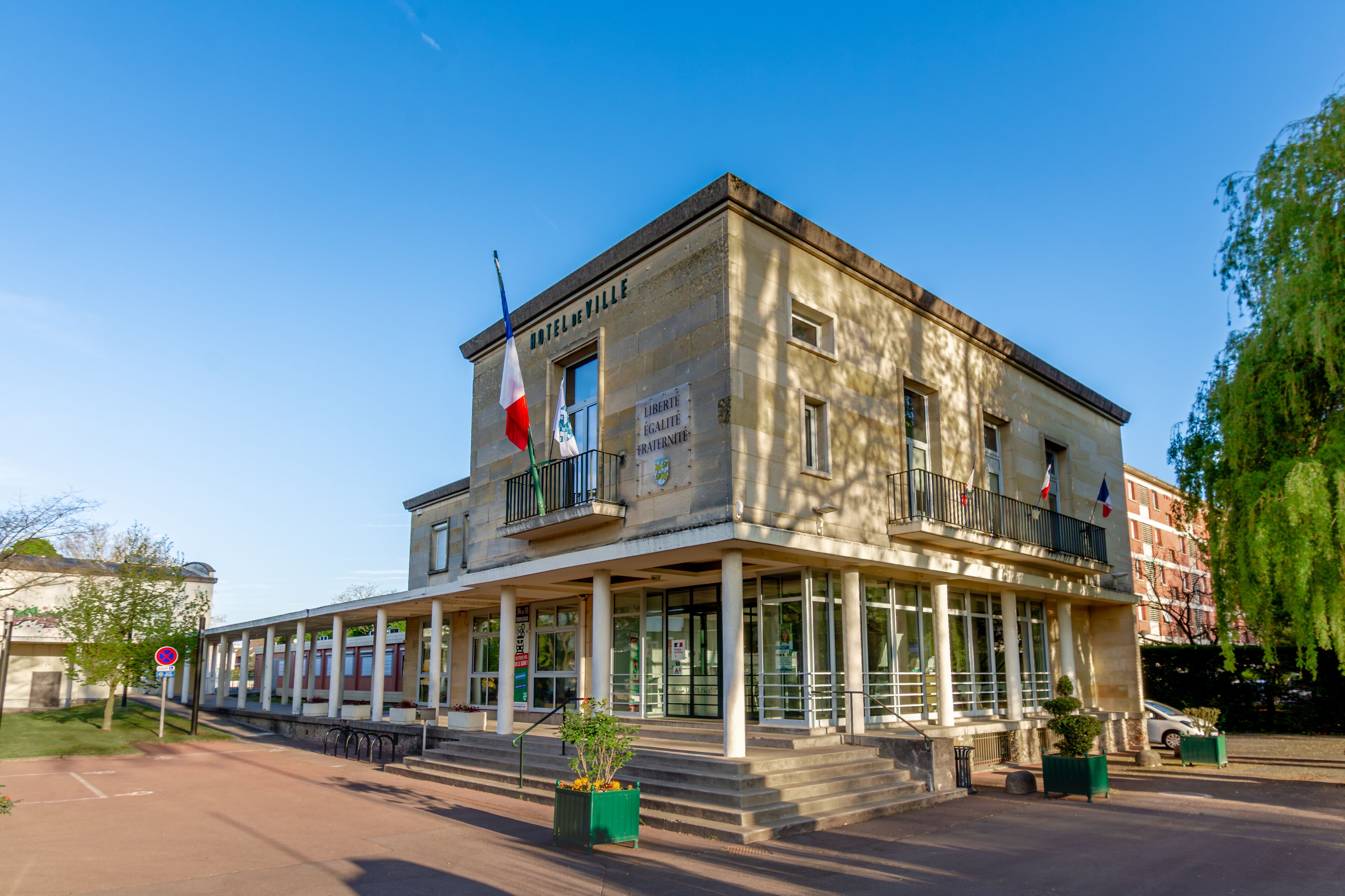 A historic building with the sign "HOTEL DE VILLE" and French flags.