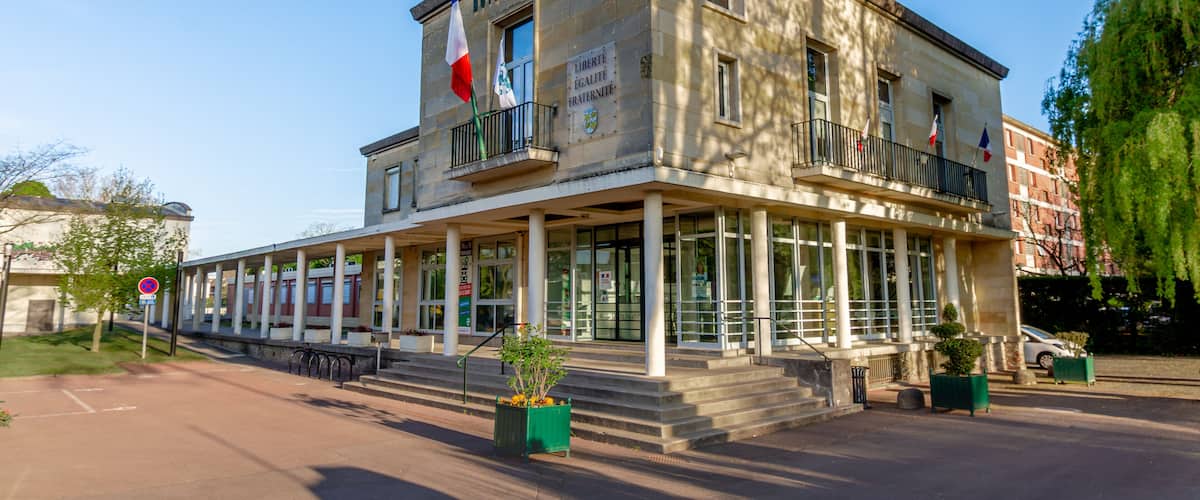 A historic building with the sign "HOTEL DE VILLE" and French flags.