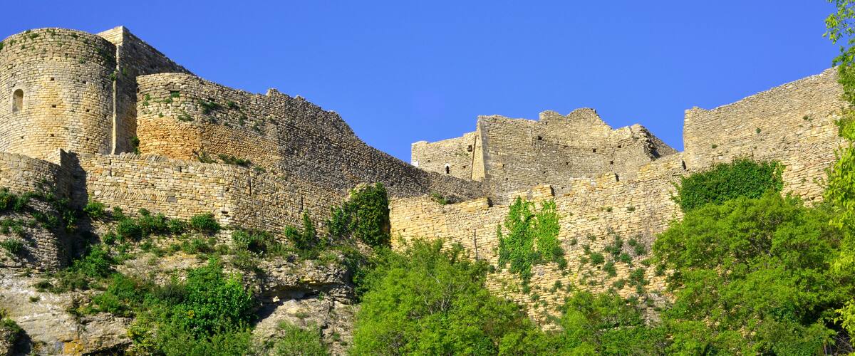 A medieval stone fortress with battlements and towers, surrounded by lush greenery.