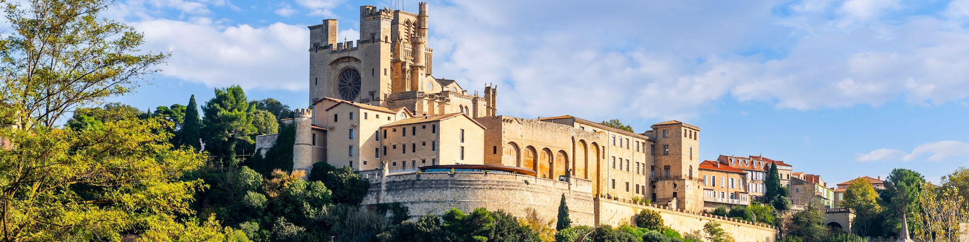 A historic castle with a prominent tower and a large circular window, surrounded by lush greenery and traditional buildings.