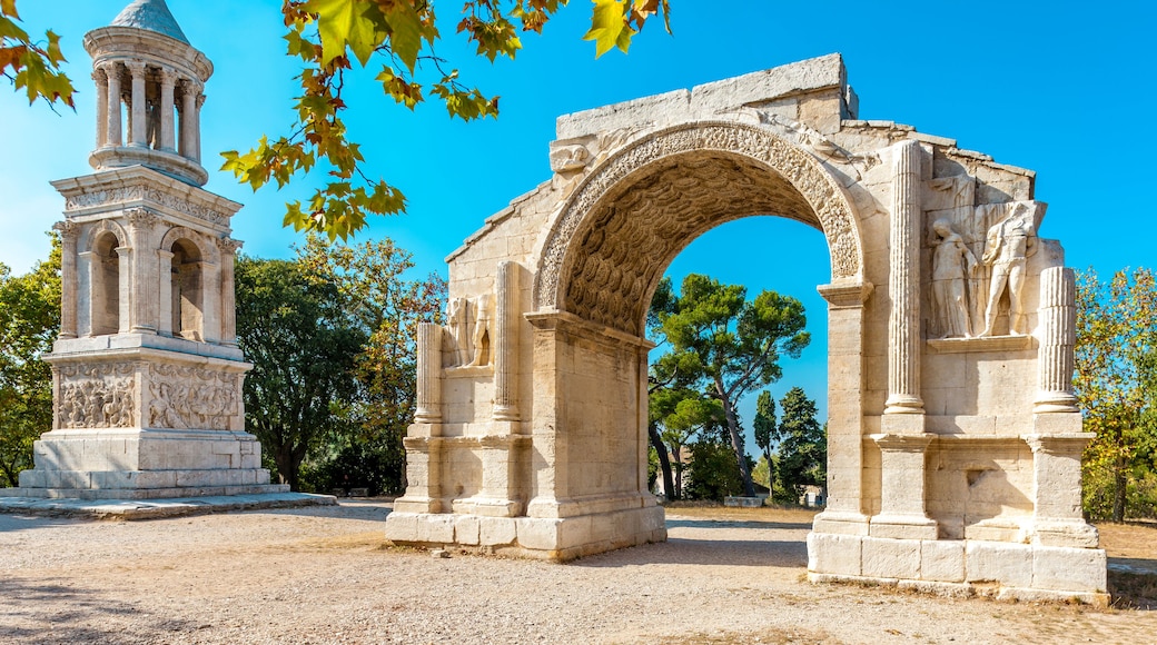 An ancient stone archway with intricate carvings, a classical column structure, and a clear blue sky.