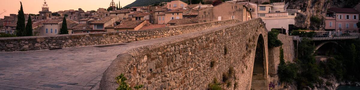 A stone bridge, a river, and a town with buildings and a hill in the background.
