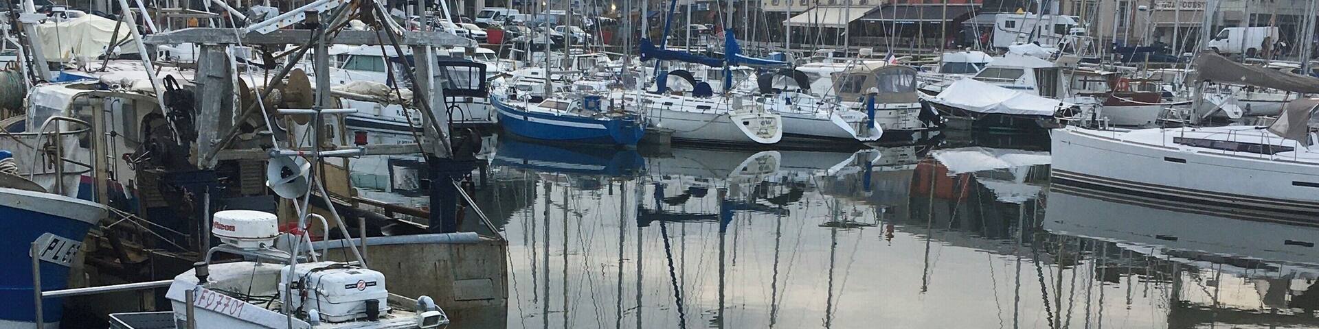 A marina with various boats docked, including a blue boat named "BAREVA" and a white boat with a striped hull.