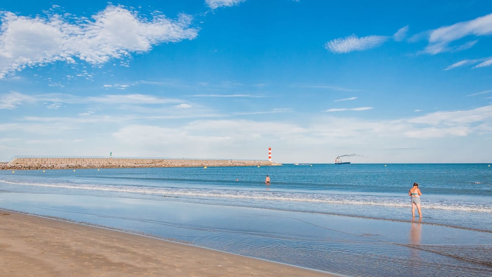 Une plage avec un phare, une mer calme et un ciel dégagé.