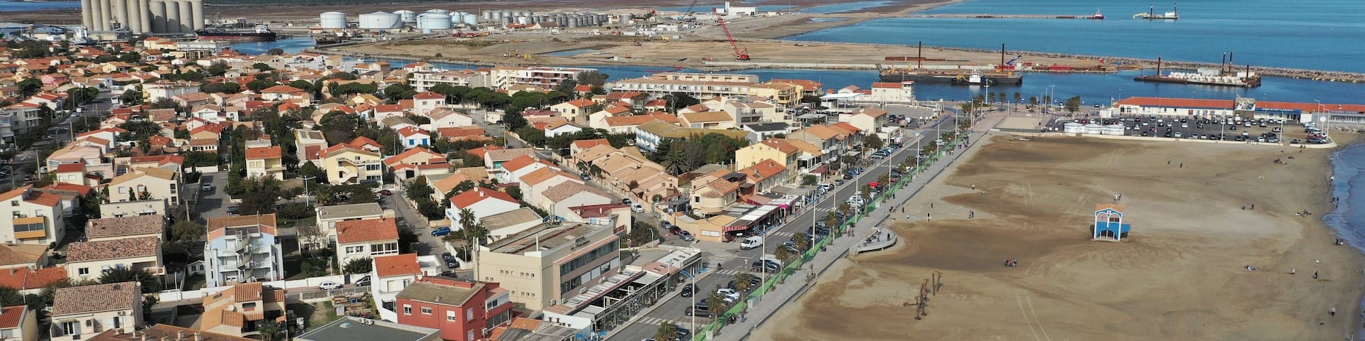 An aerial view of a coastal town with residential buildings, a beach, and industrial facilities.