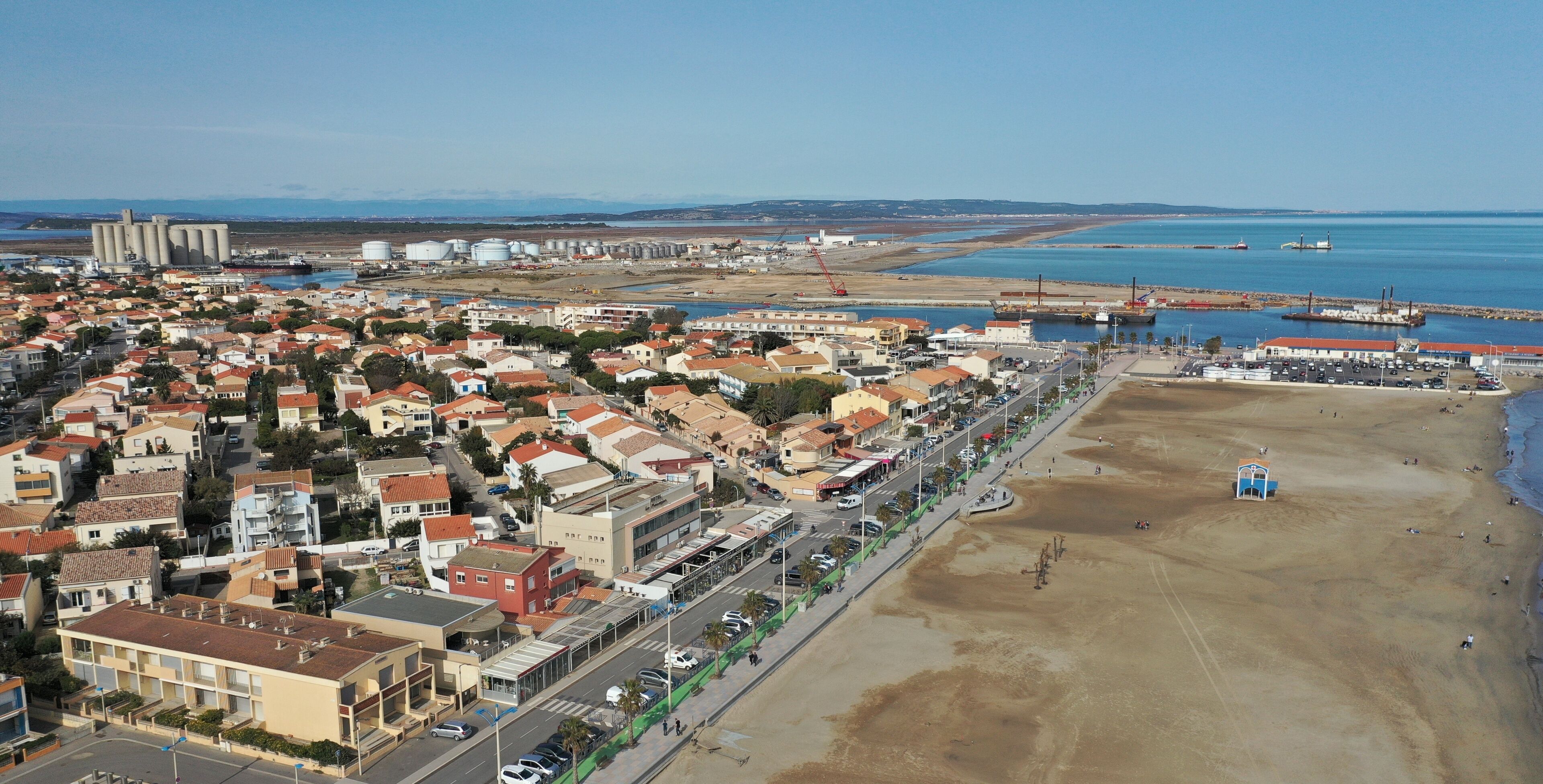 An aerial view of a coastal town with residential buildings, a beach, and industrial facilities.