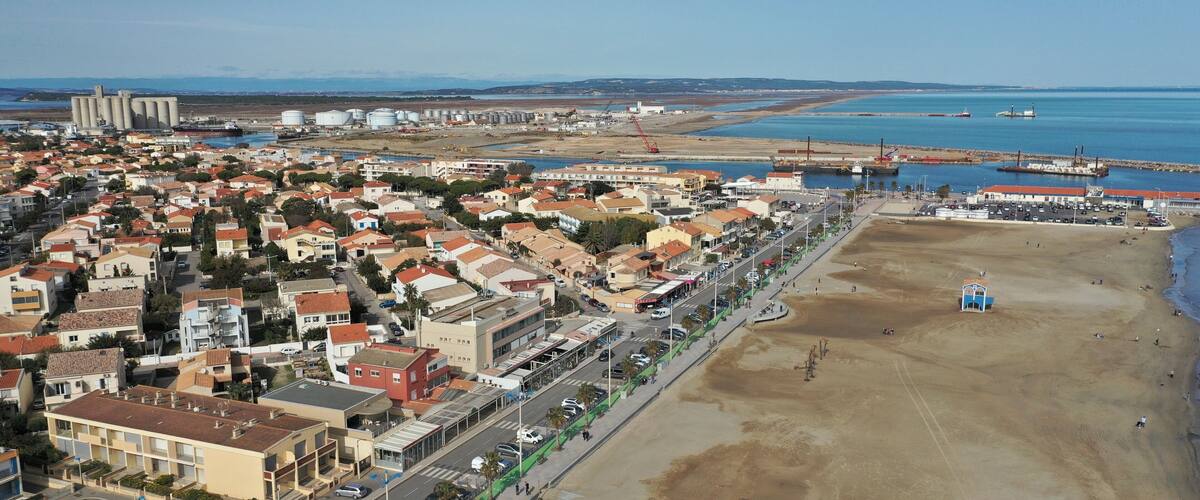An aerial view of a coastal town with residential buildings, a beach, and industrial facilities.