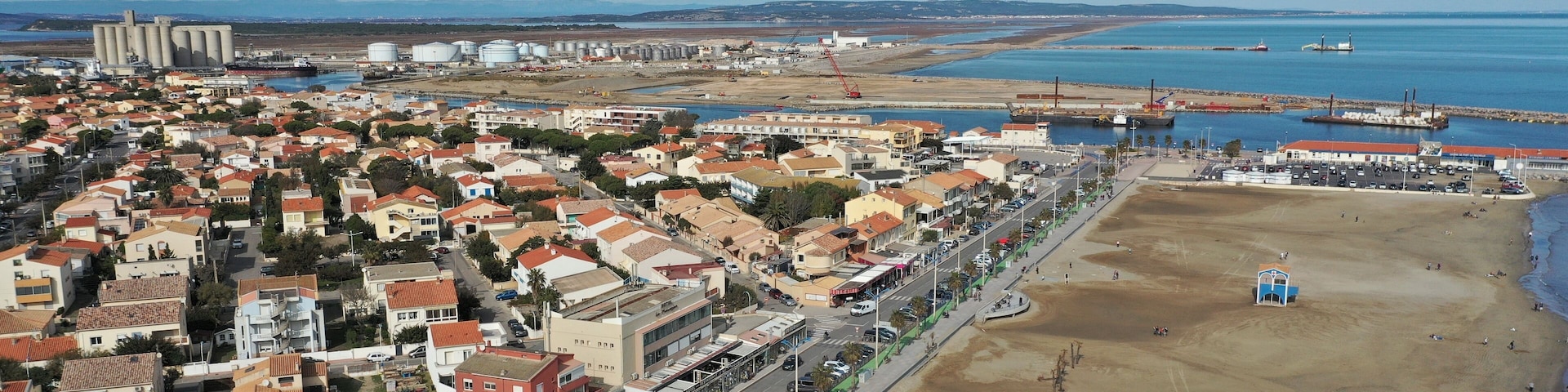 An aerial view of a coastal town with residential buildings, a beach, and industrial facilities.