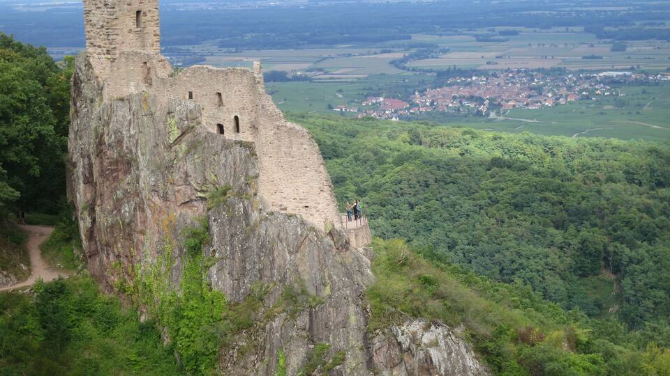 A medieval castle perched atop a rocky cliff overlooking a lush valley and a distant town.