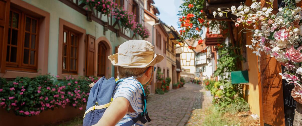A cobblestone street lined with traditional half-timbered houses, a person holding hands with another, and blooming flowers.