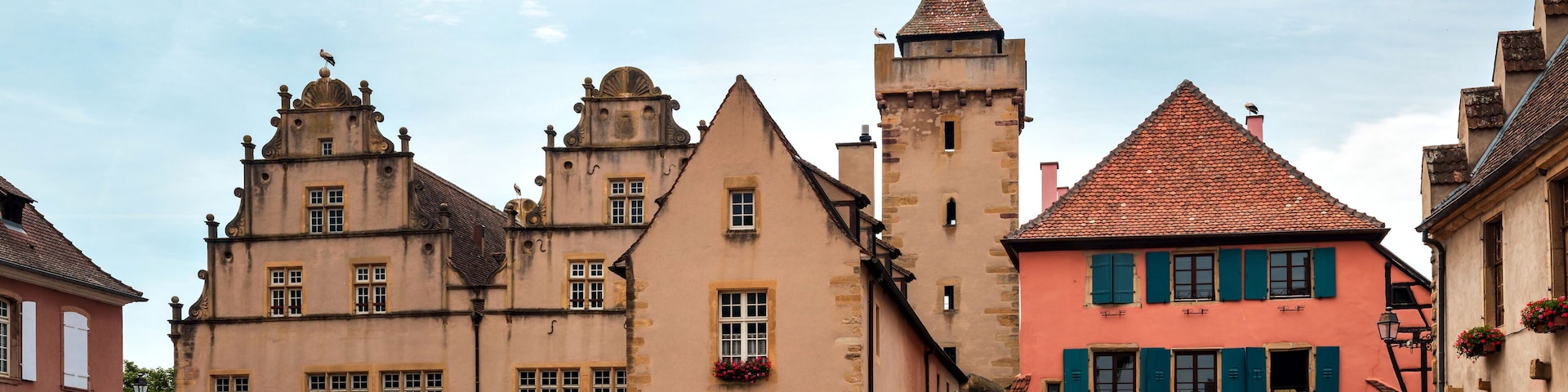 Un pueblo europeo histórico con un edificio imponente que recuerda a un castillo y una casa colorida de tejado rojo.