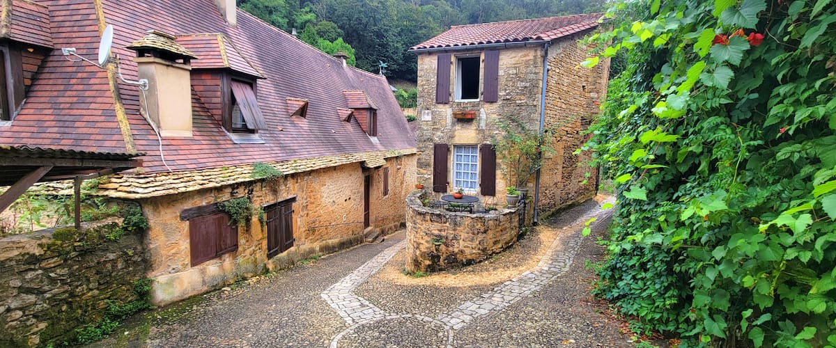 A cobblestone alley with rustic stone buildings, a stone wall, and lush greenery.