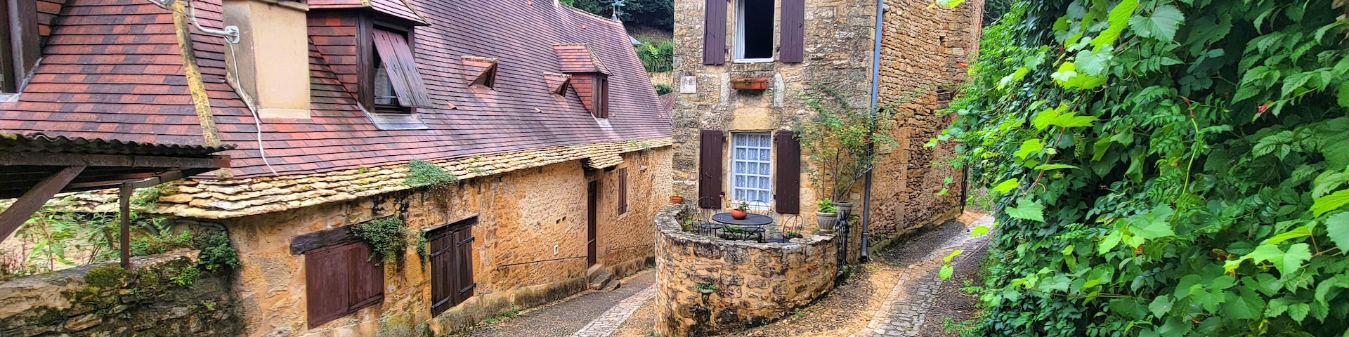 A cobblestone alley with rustic stone buildings, a stone wall, and lush greenery.
