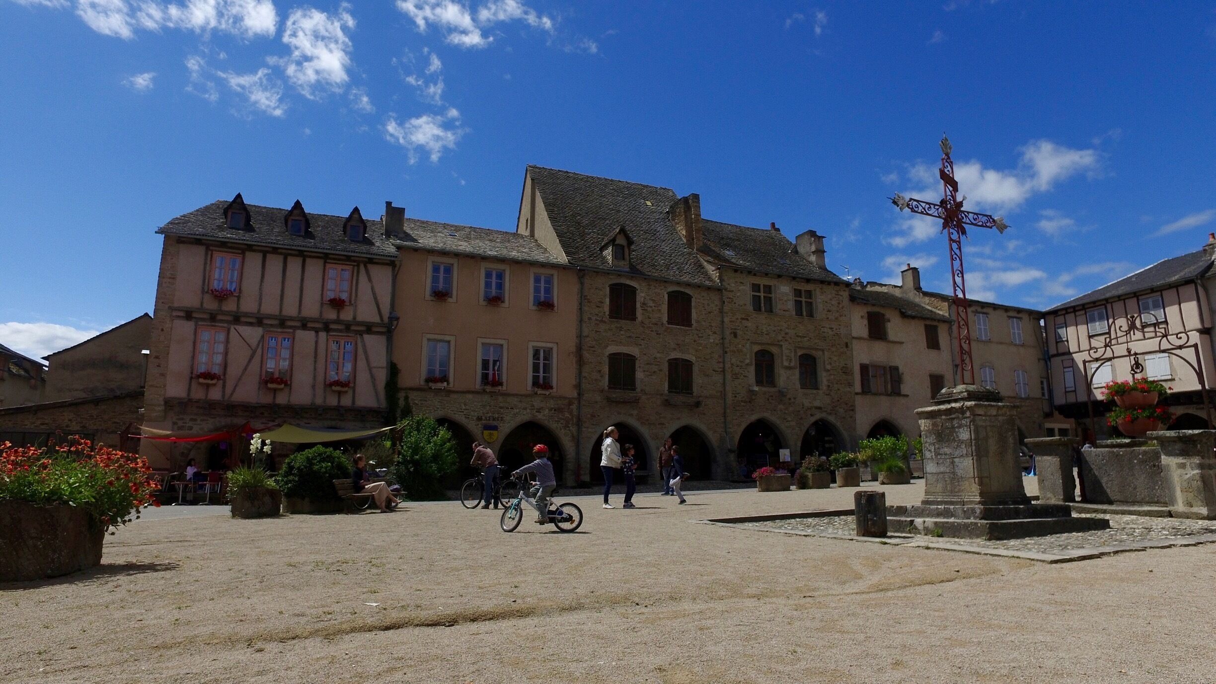A historic town square with cobblestone pavement, traditional half-timbered buildings, and a fountain.