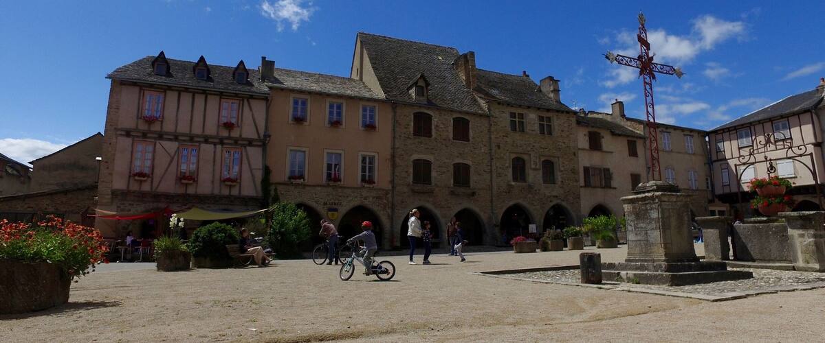A historic town square with cobblestone pavement, traditional half-timbered buildings, and a fountain.