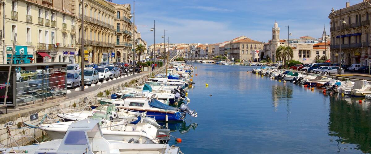 A marina with boats docked along a waterfront, surrounded by historic buildings and a clear sky.