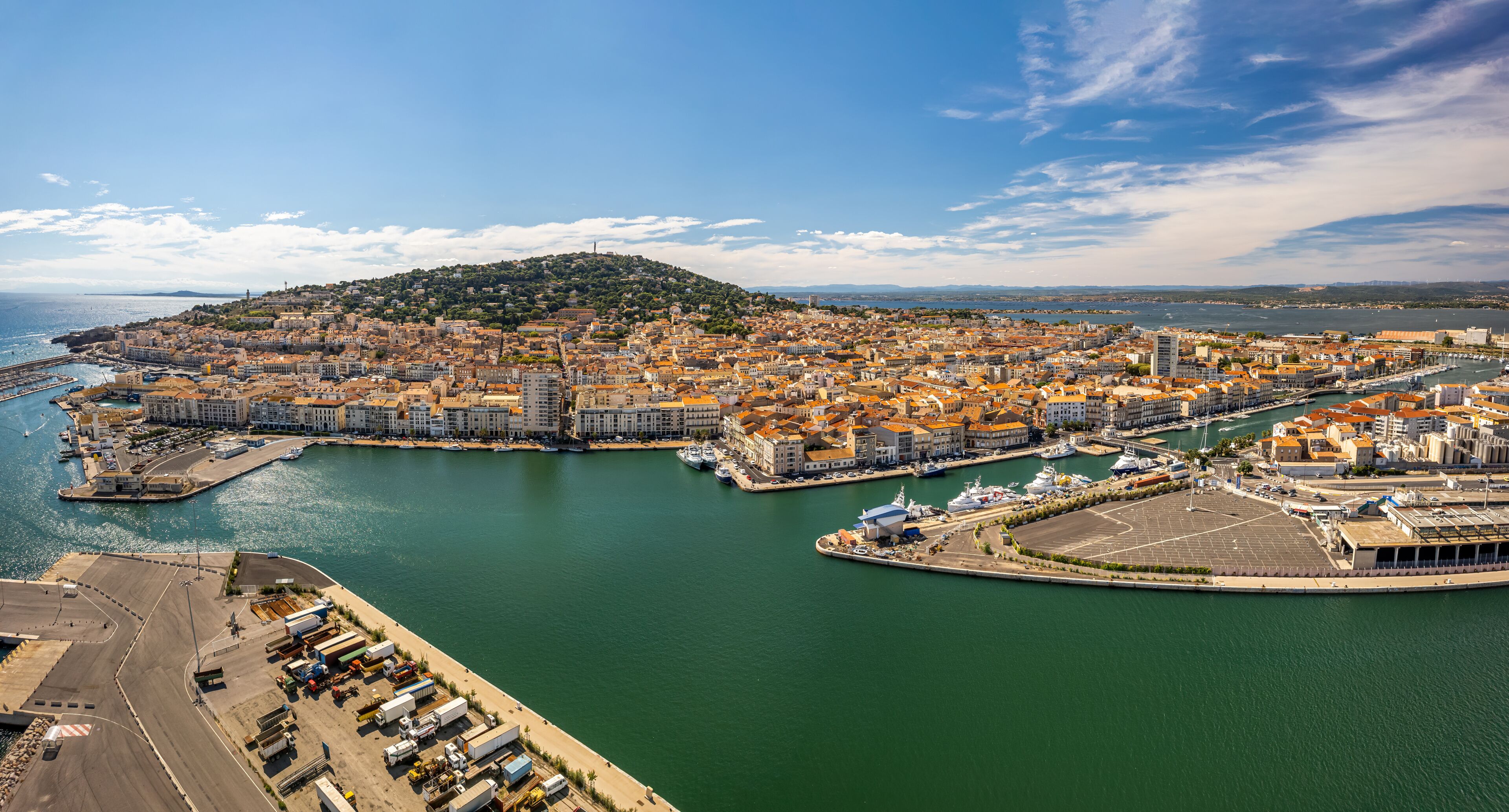 A coastal cityscape with a harbor, a hilltop, and a clear sky.