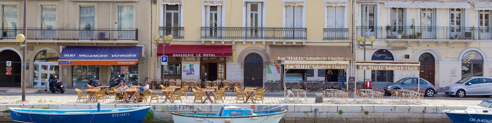 A waterfront with boats, a café, and buildings with shops.