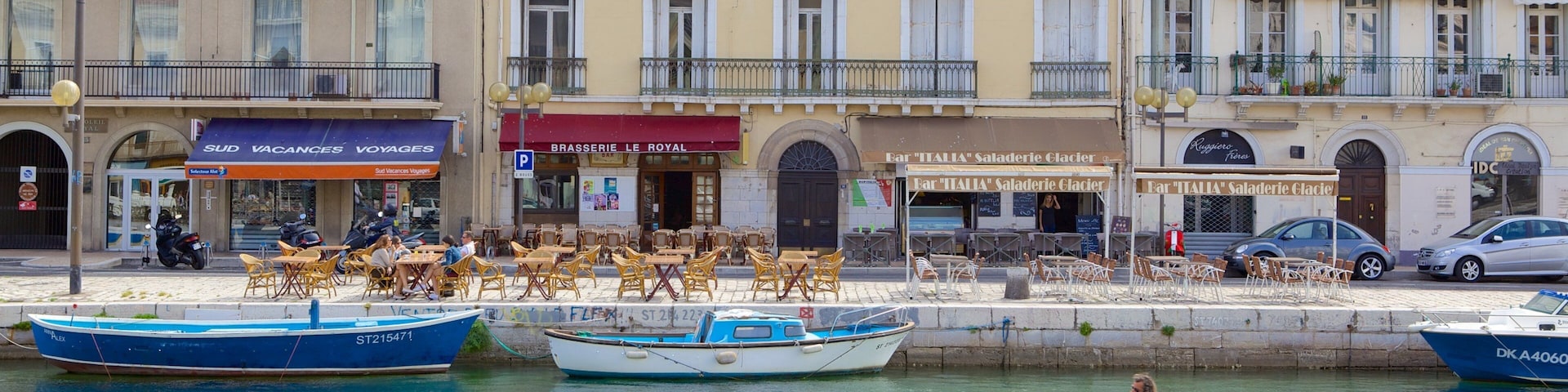 Un paseo marítimo con barcos, un café y edificios con tiendas.