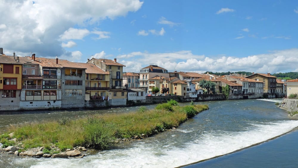 Une rivière traverse une ville où se dressent des bâtiments aux couleurs vives et un pont de pierre.