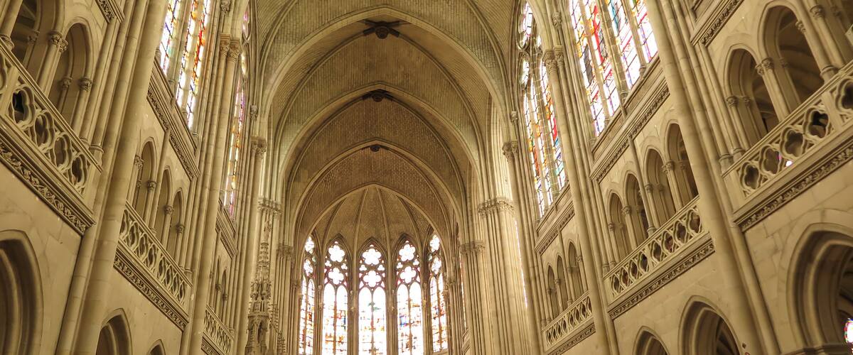 A cathedral interior with high vaulted ceilings, large stained glass windows, and intricate stone carvings.