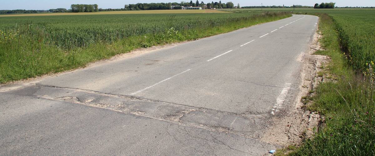 A rural road curving through green fields with a clear sky.