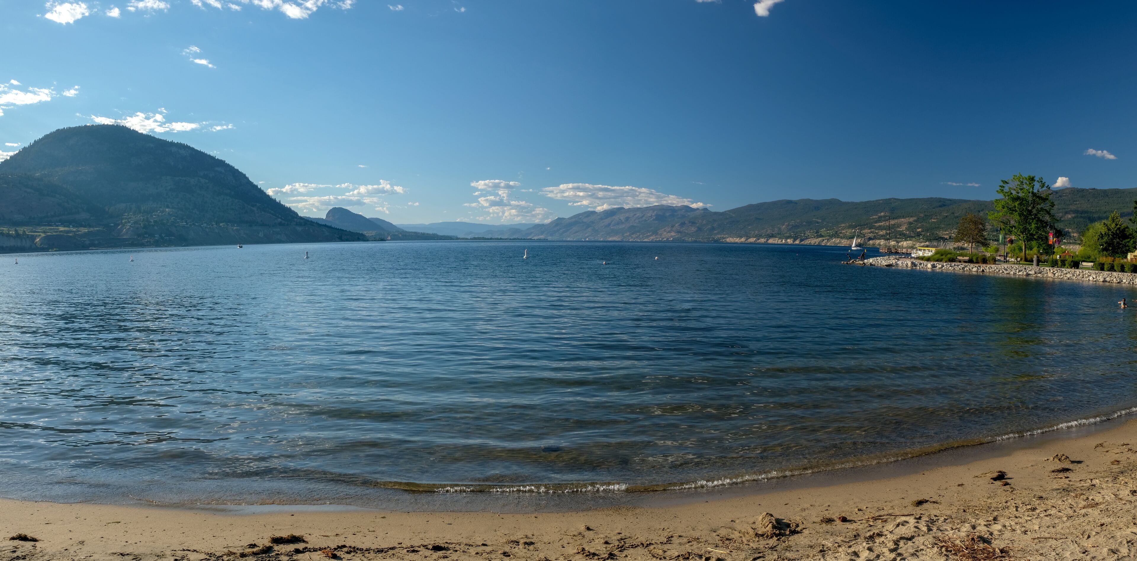A calm lake with clear water, a sandy beach, and mountains in the background.