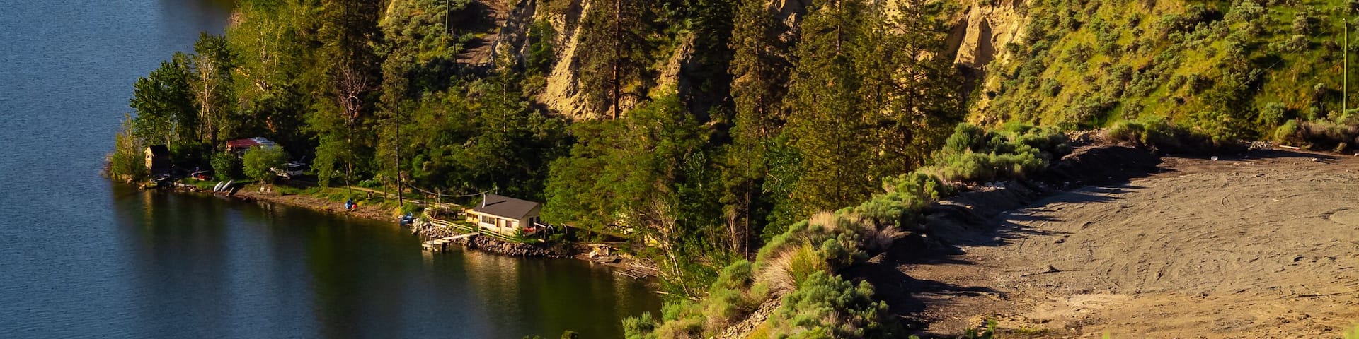 A coastal landscape with a body of water, terraced vineyards, and a steep hillside.