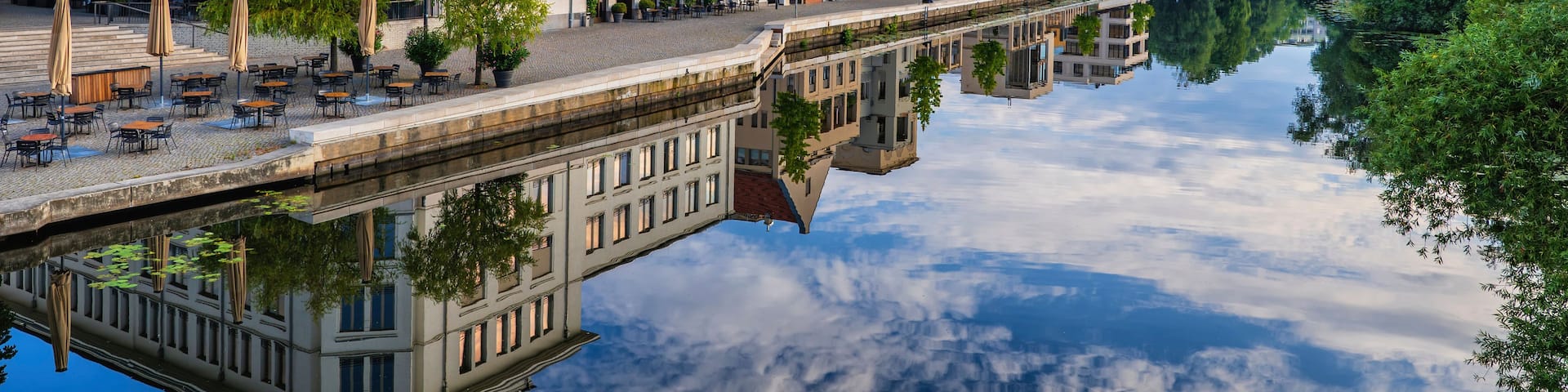 A river reflecting buildings, a green dome, and a bridge.