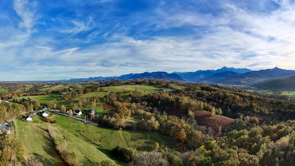 A panoramic view of a valley with rolling hills, a river, and distant mountains under a partly cloudy sky.