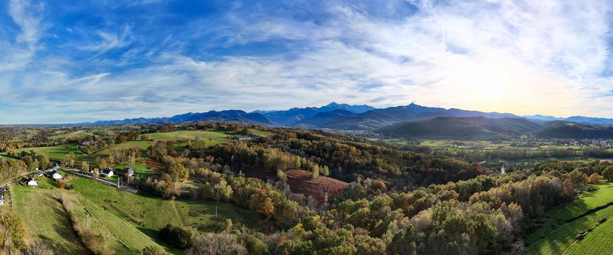 A panoramic view of a valley with rolling hills, a river, and distant mountains under a partly cloudy sky.