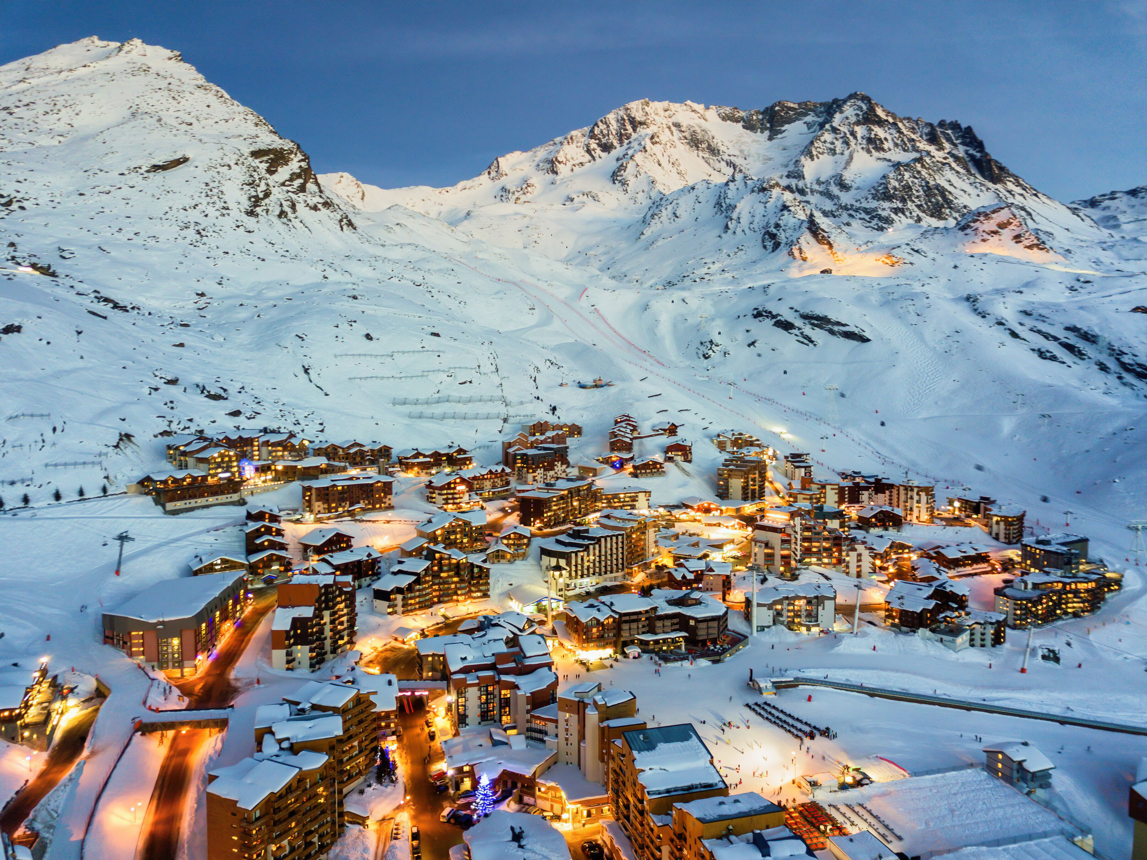 Un pueblo cubierto de nieve al anochecer, con edificios iluminados y pistas de esquí.