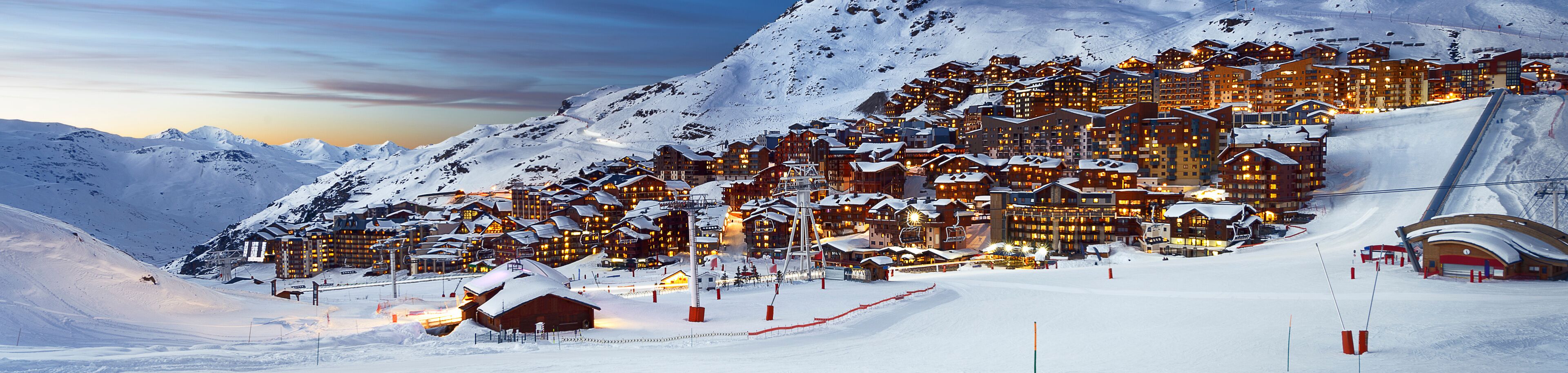A snow-covered mountain resort with illuminated buildings and ski lifts.