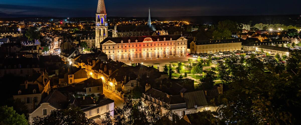 A cityscape at night with illuminated buildings, a prominent church tower, and a large historic building.