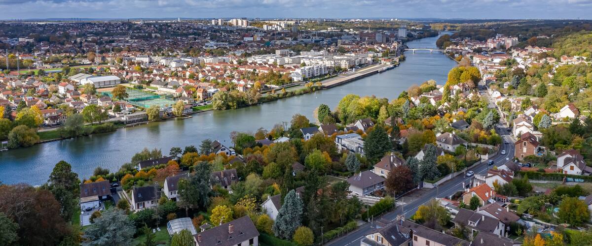 A river winding through a town with autumn foliage, a bridge, and distant buildings.