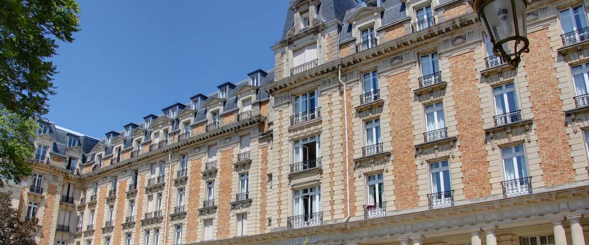 A large, historic building with multiple balconies and columns, surrounded by a well-maintained garden with sun loungers.