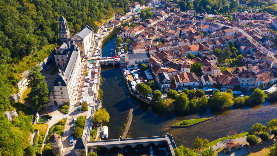An aerial view of a historic town with a river, a prominent castle, and a bridge.