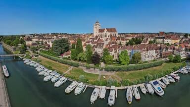 Une ville riveraine dotée de bâtiments historiques, d’une église remarquable et d’un port de plaisance où sont amarrés des bateaux.