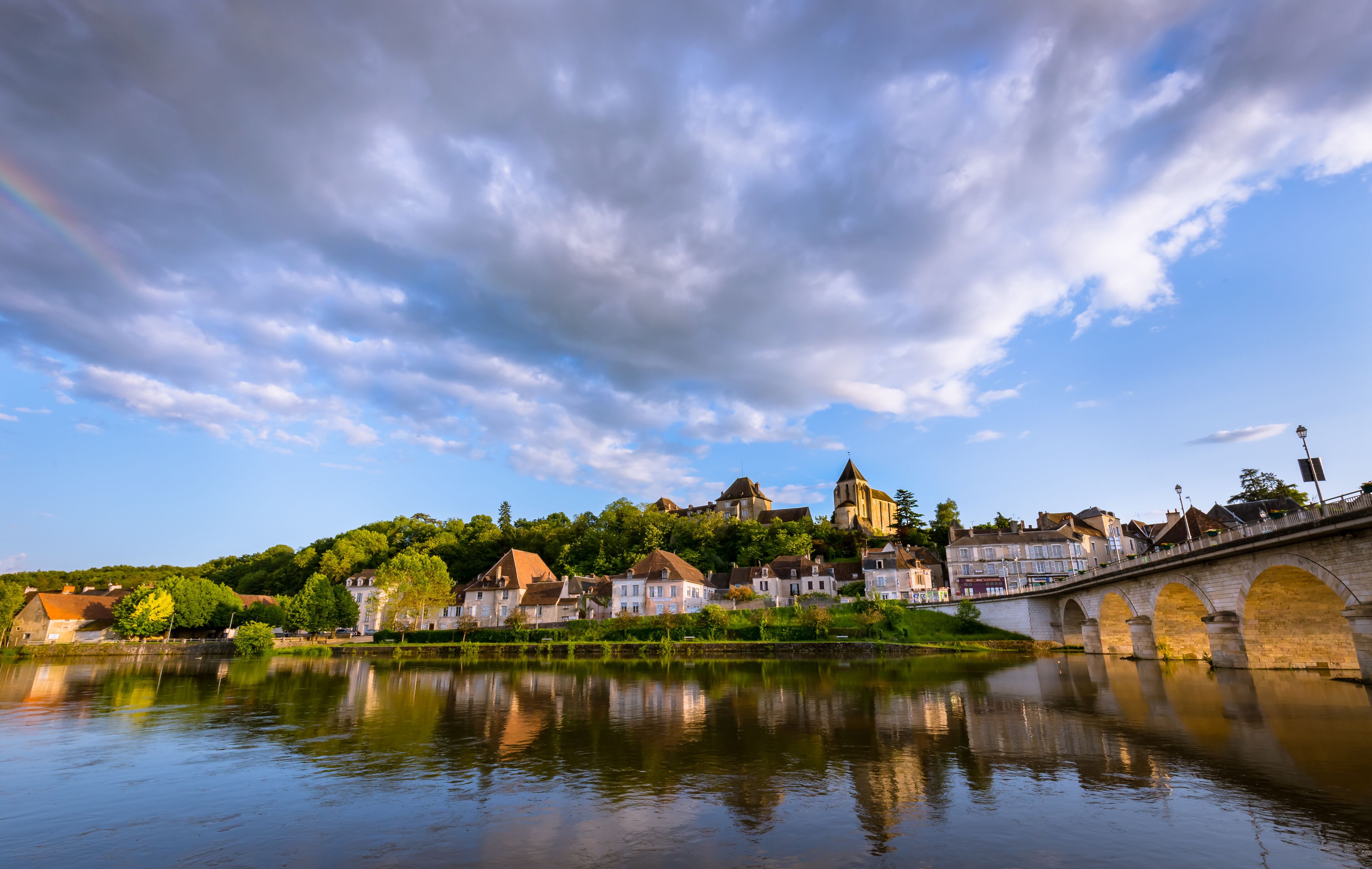 A river with a bridge, a church on a hill, and houses along the riverbank.