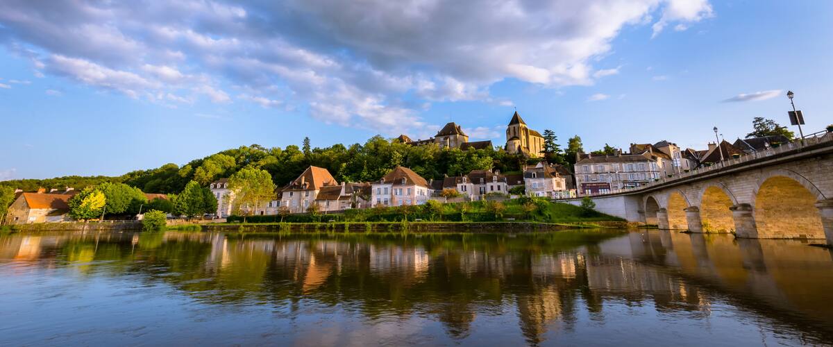 A river with a bridge, a church on a hill, and houses along the riverbank.