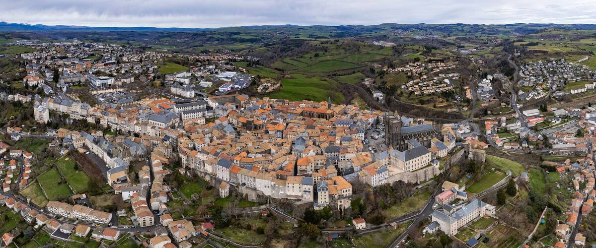 An aerial view of a historic town with a prominent castle, surrounded by rolling hills and green fields.