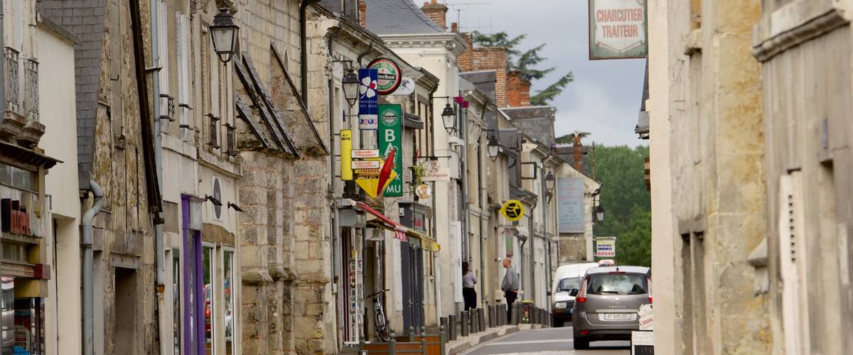 A narrow street lined with old buildings, some with signs in a foreign language, and a few parked cars.