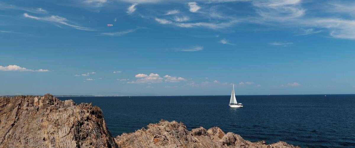 A rocky coastline with a sailboat on the sea and a clear sky.