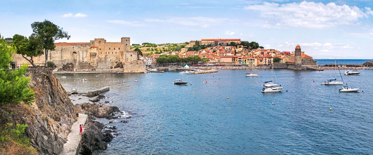 A coastal town with historic buildings, a fortified castle, and a harbor with boats.